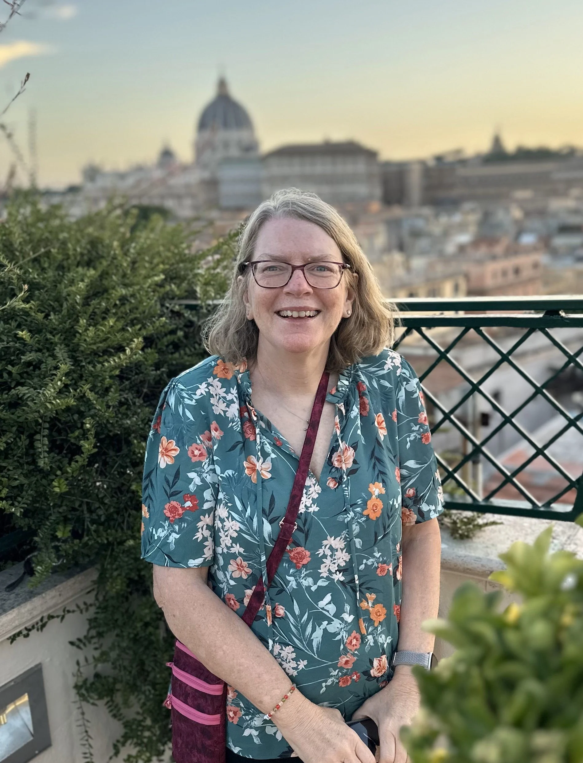 Betsy on a rooftop terrace in Rome at sunset, holding her maroon purse.